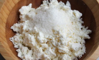 Добавьте в миску с творогом 100 грамм сахарного песка и перемешайте.