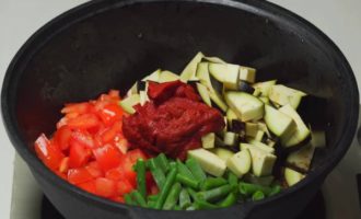 Добавьте в емкость стручковую фасоль, нарезанную крупно, нарезанные баклажаны (их нужно предварительно вымочить от горечи), а также помидоры и томатный соус. Подсолите и перемешайте мясо с овощами, тушите все вместе 5-7 минут. Огонь небольшой.