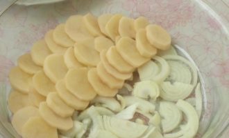 Противень или большую форму для запекания нужно смазать маслом растительным, потом первым слоем выложить лук, на лук – картофельные кружки, как показано на фото. Приправьте специями, подсолите.