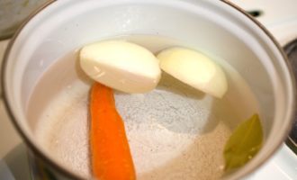 Для приготовления заливного из рыбы c желатином необходимо подготовить большую кастрюлю. В нее сложить очищенную морковь и луковицу, порезанную на четвертинки. Залить все водой, посолить и добавить лавровый лист.