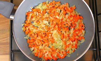 В сковороду с остатками лука добавьте нарезанную морковь и болгарский перец, а затем обжаривайте овощи на медленном огне, не забывая их перемешивать.