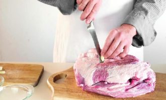 Срезать лишний жир и пленку с мясного куска. На поверхности свинины сделать прокол длинным ножом и, не доставая его, повернуть так, чтобы получилось углубление. В дырку вставить чеснок. Так нашпиговать весь кусок.