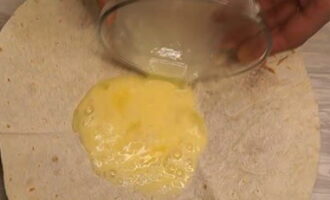 Куриное яйцо разбейте в небольшую емкость, добавьте соль и черный молотый перец по вкусу. С помощью вилки или венчика перемешайте до однородной консистенции. Лист лаваша выложите в тарелку и в получившееся углубление вылейте взбитое куриное яйцо.