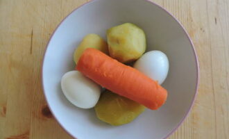Сначала промываем и отвариваем до готовности картофелины, морковь, яйца и охлаждаем их. Готовим порционную посуду для подачи салата или общее блюдо. Охлажденный картофель очищаем от кожуры, измельчаем на крупной терке и укладываем его в первый слой салата.
