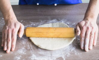 Готовое тесто посыпаем небольшим количеством муки, чтобы оно не прилипало к столу или рукам. Скалкой раскатываем в аккуратную тонкую основу.