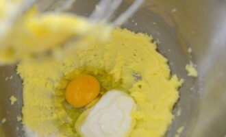 Затем выложите необходимое количество сметаны, разбейте куриное яйцо, добавьте соль и тщательно перемешайте миксером.