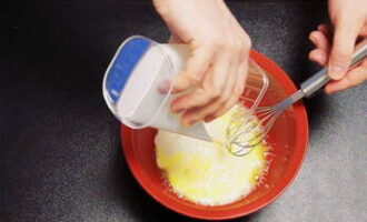 В глубокую миску разбиваем два куриных яйца. Сюда же вливаем кефир, воду и добавляем соль с сахаром. Взбиваем венчиком.