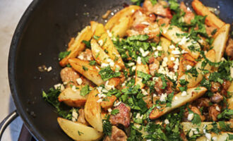 Обжаренный картофель переложите в сковороду к мясу и луку, также добавьте к ингредиентам измельченный чеснок и рубленую зелень.