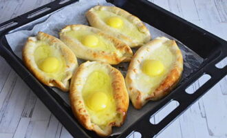 Затем достаньте хачапури из духовки и в каждую лодочку разбейте по одному яйцу. Верните противень в духовку на 3-4 минуты.