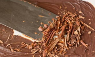 Достаньте из холодильника застывший шоколад. При помощи широкого шпателя или ножа сделайте крупную стружку. Оставшийся шоколад настрогайте овощечисткой в более мелкую крошку.