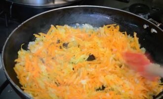 К луку добавьте тертую морковку, тщательно перемешайте. Огонь уменьшите до среднего и продолжайте обжаривать, периодически помешивая.