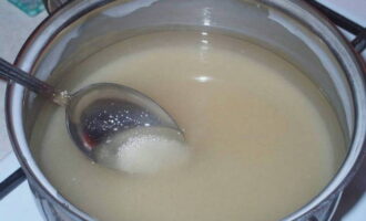 После этого из банки сливаем абрикосовую жидкость в кастрюлю. Добавляем в нее сахар и перемешиваем. Получившийся сироп доводим до кипения и варим 5 мин. 