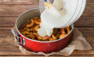 Извлекаем из холодильника смазанную маслом форму и наполняем абрикосами. Равномерно распределенные фрукты заливаем готовым тестом и отправляем выпекаться на протяжении 30 минут в заранее разогретую до 180 градусов духовку.