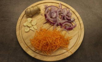 Лук нарежьте полукольцами, морковь натрите на терке, корень имбиря и чеснок нарежьте тонкими пластинками. Подготовленные ингредиенты выложите на сковороду и жарьте в течение пары минут.