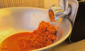 Как заготовить аджику по классическому рецепту на зиму? Необходимое количество томатов, перца чили и болгарского перца промываем в теплой воде. Чтобы не ждать в течение долгого времени, пока стечет влага, пропитываем их полотенцем. Острым ножом вырезаем все лишние детали овощей: сердцевину и «хвостики» из перца, плодоножки и места их крепления у томатов. Нарезаем перец и помидоры кусочками и отправляем в мясорубку. Измельчаем в кашицу. 