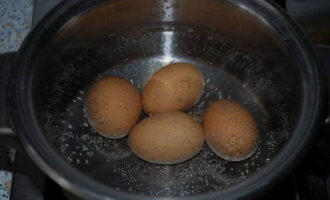 Необходимое количество яиц закладываем в другую кастрюлю. Заливаем их водой. Ставим емкость на соседнюю конфорку и провариваем яйца. Когда вода закипит, продолжаем процесс варки еще 7 минут.