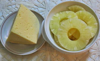 Открываем банку с ананасами и сливаем сок. Выкладываем ломтики на разделочную доску и нарезаем кубиками. Следом измельчаем сыр такими же по размеру кубиками. 