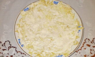 На подходящую по объему тарелку или в подставную тарелку, если салат будет готовиться порционно, выложить слой картофеля, который нужно слегка посолить и поперчить, а затем не слишком густо покрыть майонезом. 