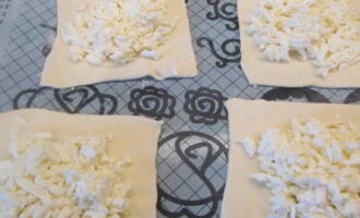 Тесто нарежьте квадратами одинакового размера. Сыр натрите на терке, смешайте его с яичным белком. На каждый квадрат теста положите сырную начинку.