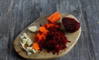 Овощи помойте и очистите. Свеклу натрите на крупной терке, морковь нарежьте тонкими кружочками, чеснок – пластинками.