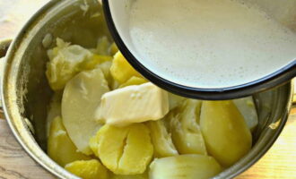 С готового картофеля слейте воду, добавьте сливочное масло и влейте горячее молоко.