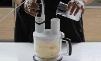 Во время измельчения ингредиентов постепенно вливаем ледяную воду. Тесто должно получиться крупчатым, легко отделяться от стенок чаши и скатываться в ком.