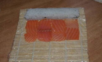 Затем рядом с роллом разложите нарезанную красную рыбу. Она может покрыть всю поверхность ролла или только с трех сторон.