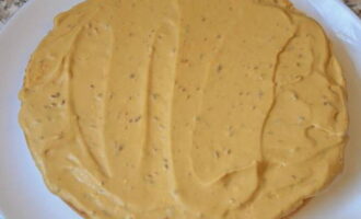 Для формирования торта возьмите плоское блюдо и уложите на него бисквитный корж. На корж ровным слоем нанесите часть крема.