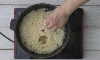 Когда рис впитает всю жидкость, вдавите в него (только до половины) две головки чеснока, сделайте огонь минимальным и тушите плов под закрытой крышкой.