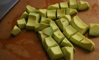 Тарталетки с авокадо приготовить очень просто. Авокадо хорошо промываем под проточной водой, обсушиваем на бумажном полотенце, после чего разрезаем его пополам, удаляем косточку при помощи ножа, очищаем от кожуры и нарезаем произвольными кусочками. Важно выбрать плод с яркой мякотью без тёмных пятен, чтобы начинка получилась красивого цвета.