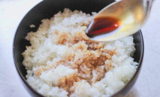 Отварной рис перекладываем в глубокую миску. Вливаем к нему три ложки соевого соуса. 