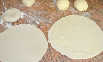 Теперь делим тесто на небольшие кусочки и катаем из каждого шарики. Из каждого, при помощи скалки раскатываем лепёшки, после чего накрываем их полотенцем, чтобы они не высохли, пока варится картофель.