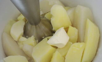 У готовой картошки сливаем воду в отдельную ёмкость. Теперь в картофель добавляем сливочное масло, берём блендер и взбиваем всё в пюре.