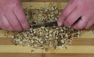 Раскалываем грецкие орехи и извлекаем из скорлупы съедобную часть. Промываем орешки и выкладываем на бумажное полотенце, чтобы впиталась лишняя влага. Мелко нарезаем продукт.