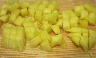 Из банки с консервированными ананасами сливаем сироп и нарезаем фрукт небольшими кубиками.