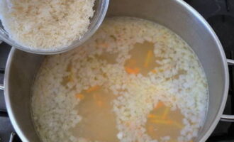 Рис хорошо промываем под проточной водой до прозрачности и добавляем его в кастрюлю с бульоном и овощами. Затем добавляем ещё немного соли, чёрный молотый перец и всё перемешиваем. Варим суп примерно 20 минут, пока не будут готовы рис с картофелем. 