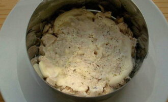 Все компоненты делим на количество порций и приступаем к сборке салата. На дно блюда выкладываем филе и промазываем ароматной заправкой.