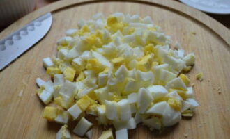 Отваренные вкрутую яйца очищаем от скорлупы, нарезаем небольшими кубиками и добавляем в салатницу.