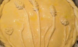 Украсьте пирог по своему вкусу, взболтайте вилкой яйцо и смажьте поверхность пирога. 