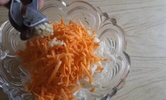 Морковь очищается, промывается и измельчается на крупной терке. Затем перекладывается к капусте. Добавляются к салату два зубка чеснока, измельченного на чесночнице.