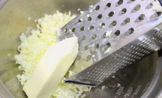 Сливочное масло для приготовления пирога должно быть замороженным. Вместо него можно использовать маргарин. Натираем масло на крупной терке в удобную для замеса теста миску. Всыпаем к маслу половину стакана сахара. Перетираем ингредиенты. Вбиваем в массу одно яйцо и перемешиваем продукты.