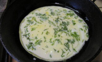 В сковородке разогреваем немного масла и выливаем половину яичной смеси, присыпаем мелко нашинкованной зеленью.