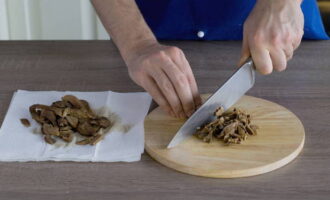 Чтобы грибы быстро обсохли, выкладываем их на бумажное полотенце. Отвар, который остался после варки грибов, процеживаем через пару слоев марли. Сами грибы нарезаем ломтиками.