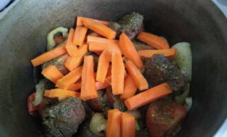 Когда помидоры пустят сок, перекладываем в чугунную посуду крупные бруски очищенной моркови. Размешиваем содержимое казана и готовим еще 5 минут.