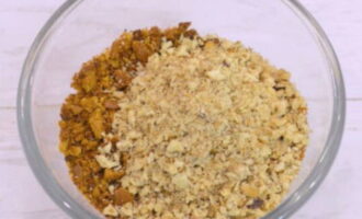 В чаше блендера перебиваем ядра грецких орехов и в отдельной тарелке смешиваем их с крошкой из коржей – мешаем.