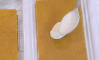 Приступаем к сборке торта: на плоское блюдо выкладываем первый корж, обильно смазываем кремом и накрываем вторым прямоугольником из теста.