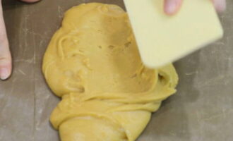 Противень устилаем листом пекарской бумаги и выкладываем на него ½ часть медового теста – разравниваем шпателем, стараясь сделать ровный слой.