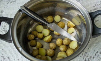 Небольшие клубни молодого картофеля заранее вымыть со щеточкой, отварить, не снимая кожуру и полностью остудить. Затем их разрезать на половинки и переложить в посуду для холодника.