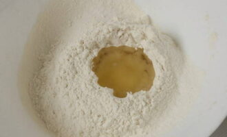 Просеянную муку горкой пересыпать в посуду для замеса теста или на столешницу и посыпать солью. В середине этой горки сделать углубление и влить в него растительного масла без запаха. 
