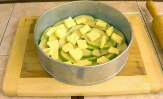 Яблочную нарезку компактно и в виде веера выкладываем в форму. Поверх яблок равномерно раскладываем нарезанное кубиками сливочное масло.